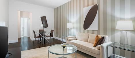 A modern living room with a glass coffee table, a beige sofa, and striped wallpaper.