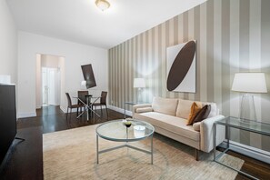 Ein modernes Wohnzimmer mit einem Glastisch, einem beigen Sofa und rauen Tapeten.