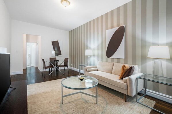 A modern living room with a glass coffee table, a beige sofa, and striped wallpaper.