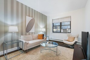 A modern living room with a sofa, two side tables with lamps, a glass coffee table, a chair, and a TV.