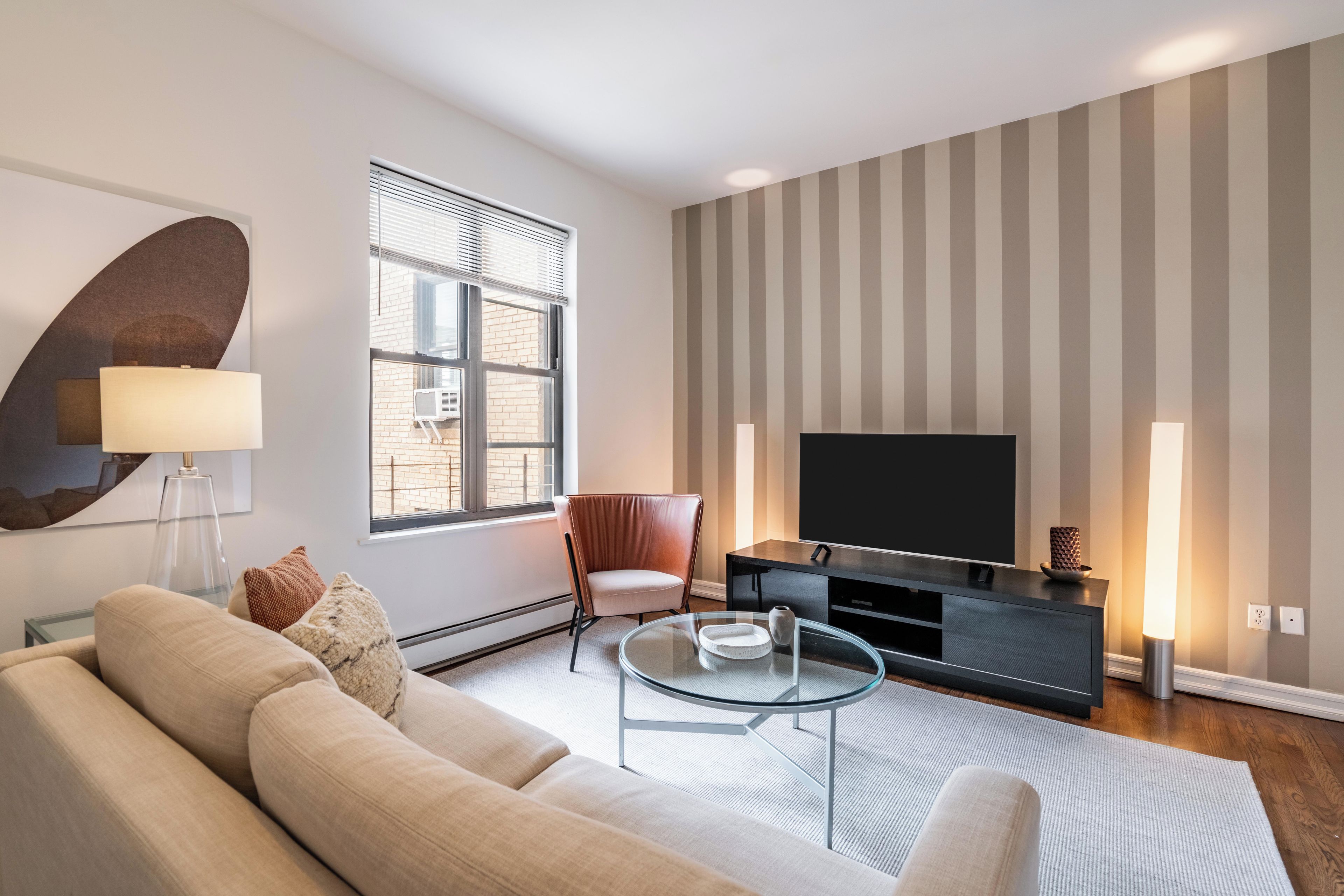 A modern living room with a sofa, a glass coffee table, a TV, and a striped wall.