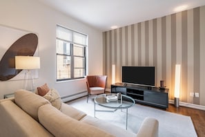A modern living room with a sofa, a glass coffee table, a TV, and a striped wall. - Culture & Comfort | UWS | Pet-Friendly (New York)