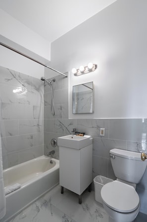 A bathroom with a bathtub, sink, toilet, and a mirror with lights. - Culture & Comfort | UWS | Pet-Friendly (New York)