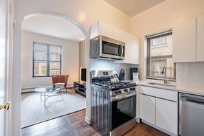 A modern kitchen with stainless steel appliances, a glass coffee table, and a view through an archway. - Culture & Comfort | UWS | Pet-Friendly (New York)
