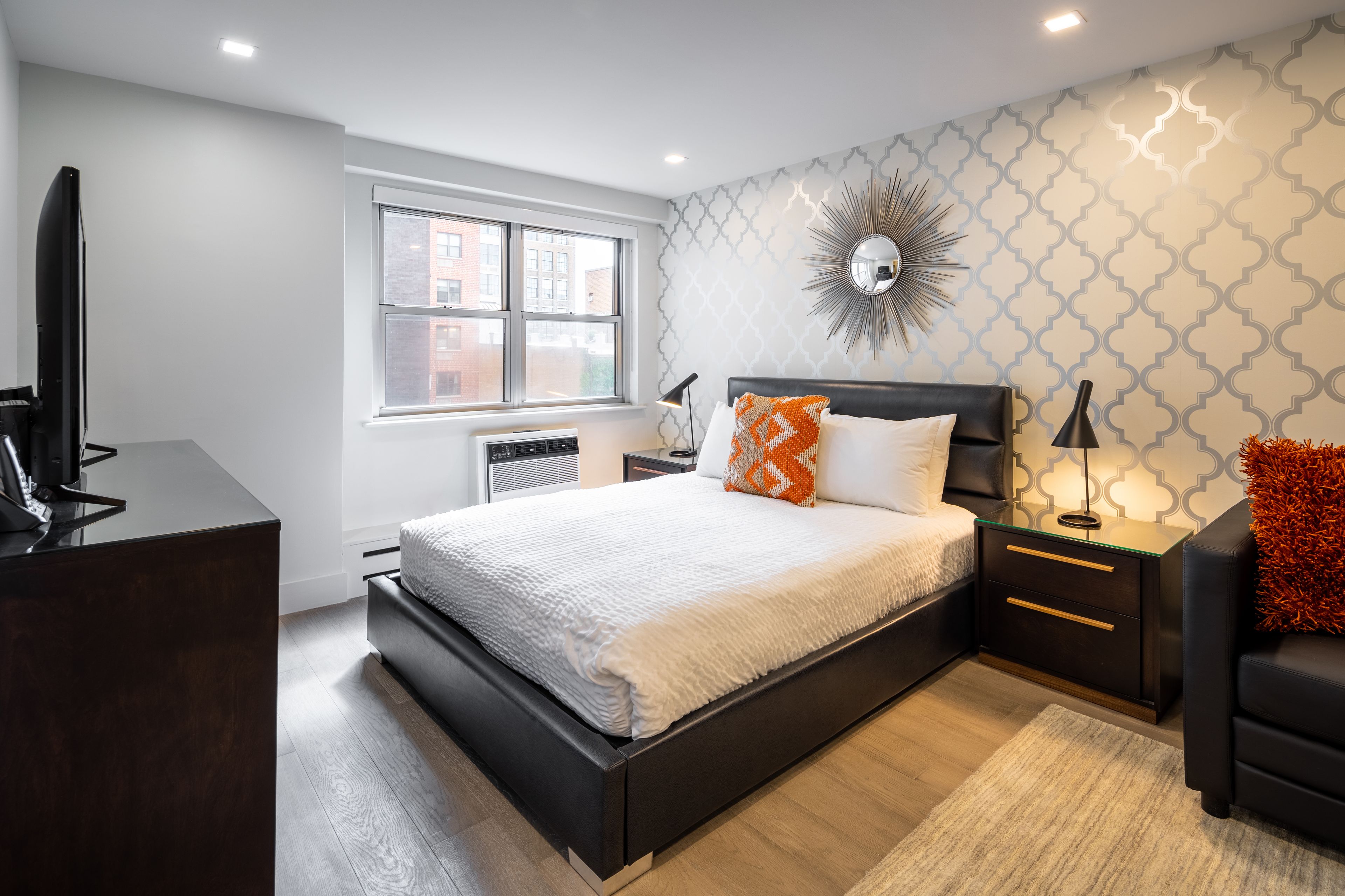 A modern bedroom with a large bed, a TV, a desk, and a window.