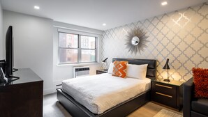 Quarto moderno com uma cama grande, televisão, escrivaninha e janela.