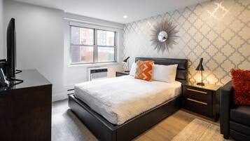 A modern bedroom with a large bed, a TV, a desk, and a window.