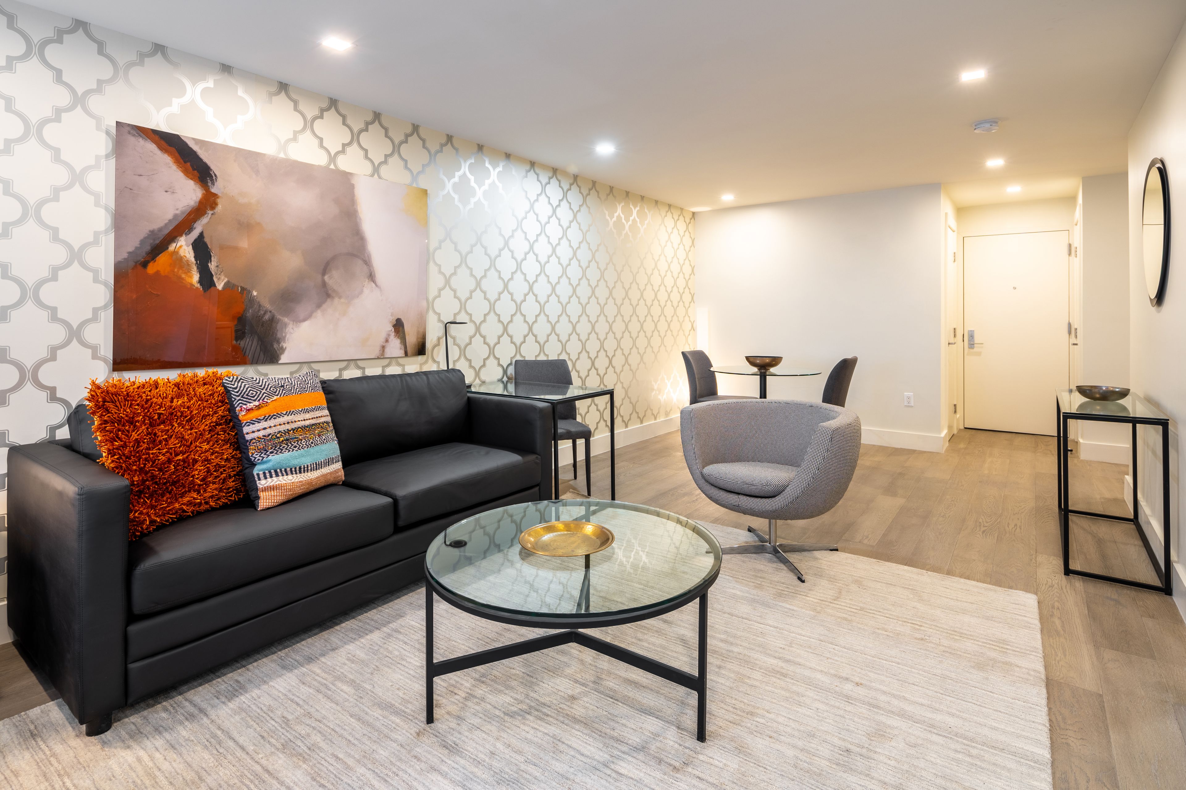 A modern living room with a black leather sofa, a glass coffee table, and a gray armchair.