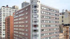 Um edifício de vários andares com entrada na esquina, um hidrante visível e uma faixa de pedestres.