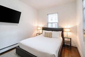 Ett hotellrum med en säng, två sänglampor, en platt-TV som är monterad på väggen och ett fönster med persienner.