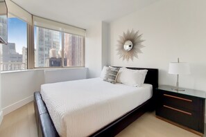 A modern bedroom with a large bed, a nightstand, a lamp, and a decorative mirror on the wall.