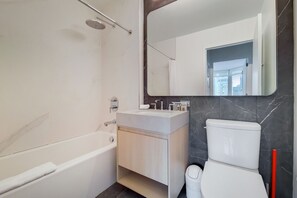 A modern bathroom with a bathtub, a vanity with a mirror, and a toilet.