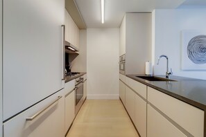 A narrow kitchen with a stainless steel sink, a stove, and a microwave.