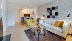 Un salon moderne avec une table basse en verre, un canapé blanc agrémenté de coussins jaunes, un fauteuil jaune et un mur à motifs.