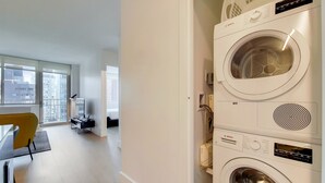 Un appartement moderne doté d’une grande fenêtre, d’un coin repas et d’un lave-linge Bosch à chargement frontal.