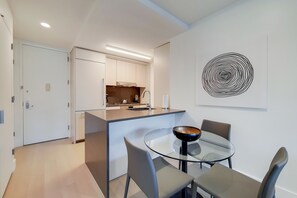 A modern kitchen with a central island, a dining area with a glass table and chairs, and a wall-mounted abstract art piece.