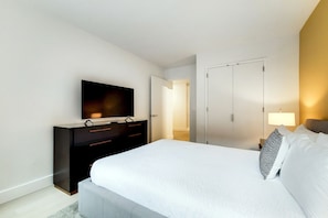 Une chambre d’hôtel moderne dotée d’un grand lit, d’un téléviseur à écran plat, d’une armoire et d’une porte donnant sur une autre pièce.
