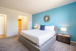 Quarto com uma cama grande, duas mesas de cabeceira com luminárias, um espelho fixado na parede e uma porta que dá para outro cômodo.