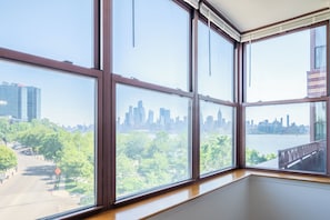 A room with large windows offering a view of a city skyline and a park. - Two Bedroom in Hoboken, Quick Access to NYC (Hoboken)
