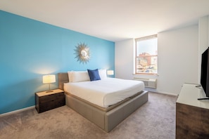A bedroom with a bed, nightstand, lamp, and a view of the city through a window. - Two Bedroom in Hoboken, Quick Access to NYC (Hoboken)