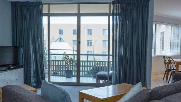 A living room with a sofa, a coffee table, a TV, and a balcony with a view of buildings.
