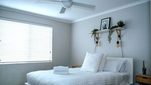 A neatly made bed with white linens, a ceiling fan, and a bedside table with a lamp.