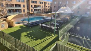 A pool area with a sunshade, lounge chairs, and a small table.