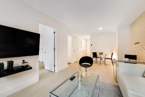 Un salon moderne doté d’un téléviseur à écran plat, d’une table basse en verre, d’un canapé blanc et d’un coin repas avec une table et des chaises.