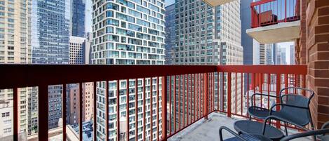 A balcony with red railings, a view of tall buildings, and two black metal chairs.