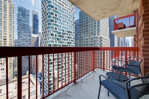 Ein Balkon mit roten Geländern, Blick auf hohe Gebäude und zwei schwarze Metallstühle.