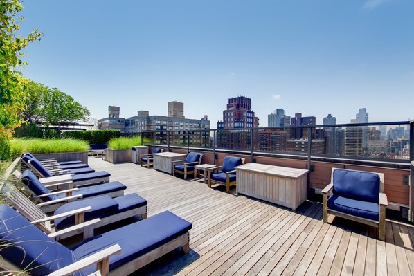 Eine Dachterrasse mit Liegestühlen, Tischen und Blick auf die Stadt.