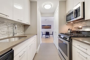 A modern kitchen with white cabinetry, a stainless steel sink, a built-in microwave, and a gas stove.