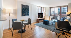 Un salon moderne avec une table en verre, deux fauteuils, un canapé, une table basse, une bibliothèque et un grand tableau abstrait.