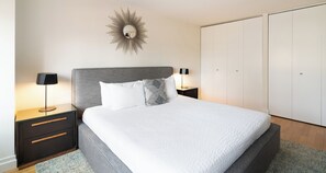 Une chambre à coucher comprenant un lit, deux tables de chevet, une commode, un miroir et une armoire.