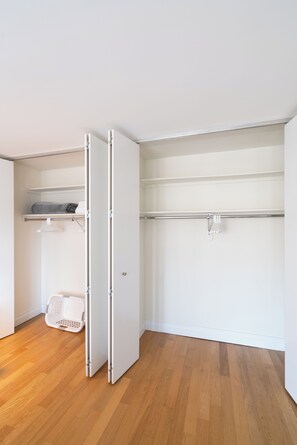 A room with a wooden floor, a white closet with a hanging rod, and a shelf with folded clothes. - Luxury Midtown Living | Balcony & Fitness Center (New York)