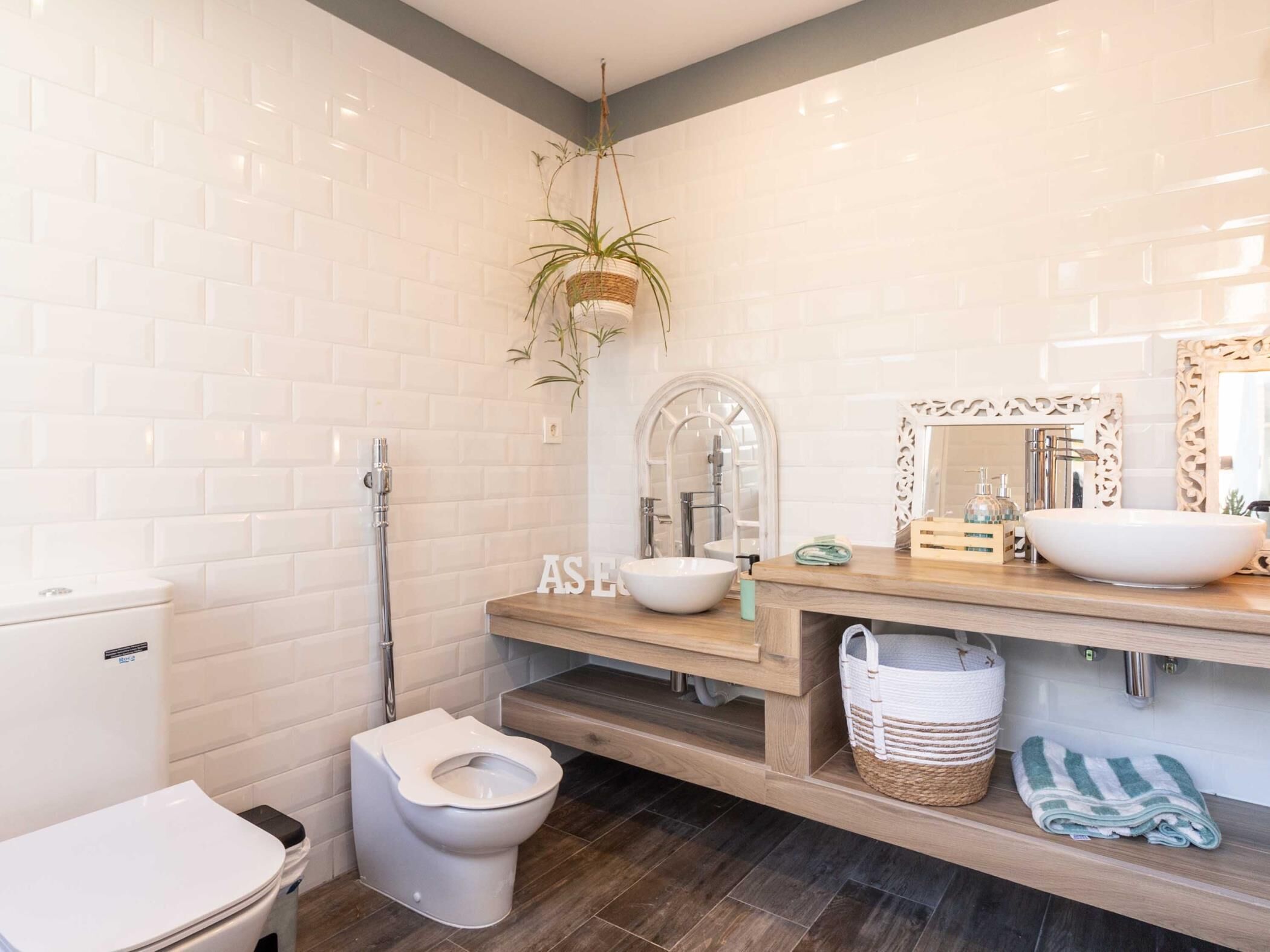 A modern bathroom with white subway tiles, a wooden vanity, a large mirror, and a hanging plant.