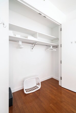 A closet with white shelves, a hanging rack, and a white laundry basket. - One Bedroom with Private Balcony in Times Square (New York)