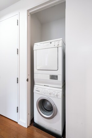 Une machine à laver et un sèche-linge superposés dans une pièce avec une porte blanche et un plancher en bois.