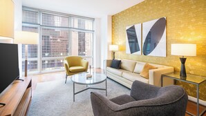 A modern living room with a sofa, armchairs, a glass coffee table, and a TV. Large windows offer a city view. - Live the Broadway Life | Times Square | W/D (New York)
