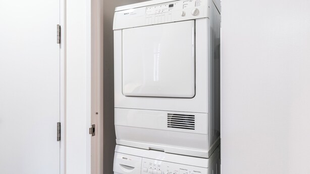 A stacked washer and dryer unit in a room with a white door and wooden flooring. - Live the Broadway Life | Times Square | W/D (New York)