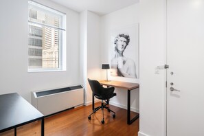 Un espacio de oficina moderno con un escritorio, una silla, un radiador, una ventana y una obra de arte enmarcada en la pared.