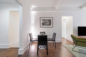 A modern dining area with a round table, two black chairs, a framed picture on the wall, and a green chair in the corner.