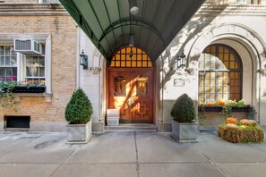 Une entrée d’immeuble avec une porte en bois, un auvent vert et une façade en briques.