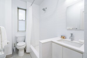 A bathroom with a toilet, shower, sink, and a window.