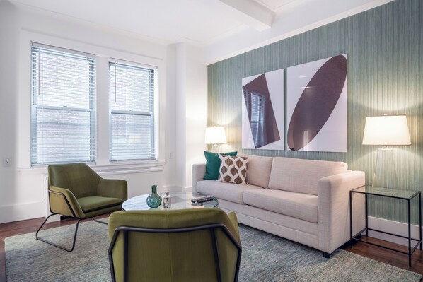 A modern living room with a sofa, two armchairs, a coffee table, and two lamps.