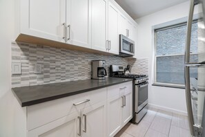 A modern kitchen with white cabinets, a microwave, a coffee maker, and a stove.