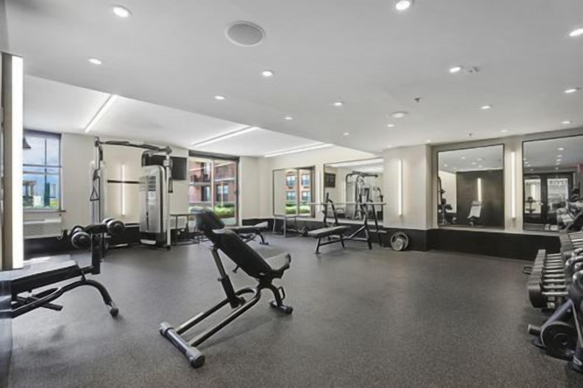 Ein Fitnessstudio mit Trainingsgeräten, Spiegeln und einem großen Fenster.