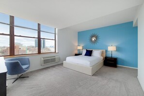 A modern bedroom with a large window, a bed with white bedding, two bedside lamps, and a blue accent wall.