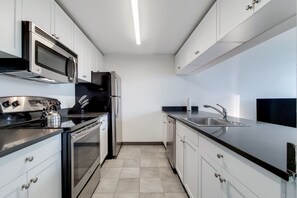 A modern kitchen with stainless steel appliances, white cabinetry, and a black countertop. - Upscale Fully Furnished Two-Bedroom in Hoboken (Hoboken)
