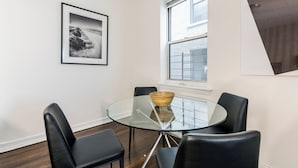 Un espace repas moderne avec une table en verre, des chaises noires et un tableau encadré accroché au mur.
